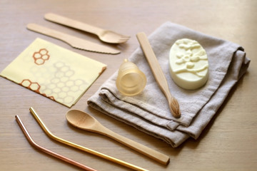 Various zero waste products on a wooden table: cloth, soap, cutlery, straws, toothbrush and menstrual cup. 