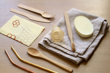 Various zero waste products on a wooden table: cloth, soap, cutlery, straws, toothbrush and menstrual cup. 