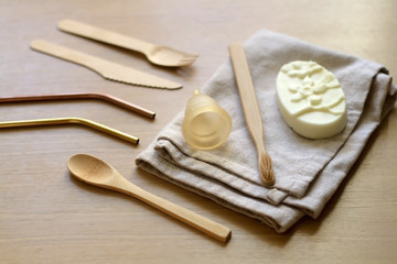 Various zero waste products on a wooden table: cloth, soap, cutlery, straws, toothbrush and menstrual cup. 