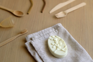 Various zero waste products on a wooden table: cloth, soap, cutlery, straws, toothbrush and menstrual cup. 