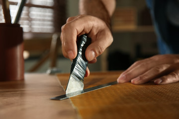 Man cutting leather with knife in workshop, closeup