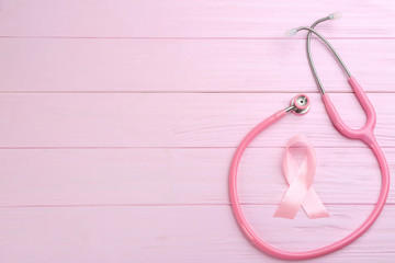 Pink ribbon and stethoscope on wooden background, flat lay with space for text. Breast cancer concept