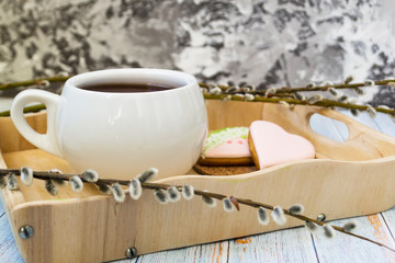 A willow twig with buds and a white cup of tea stands on a wooden tray. The concept of morning, breakfast