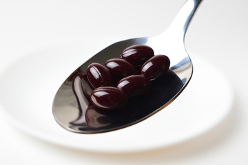 Astaxanthin capsules in the spoon on a white plate background. Close-up