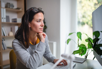 Businesswoman sitting at the desk indoors in office, using computer.