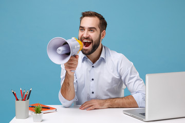 Funny young bearded man in light shirt sit work at desk with pc laptop isolated on pastel blue...