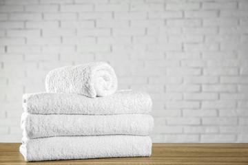 Fototapeta na wymiar Clean bath towels on wooden table near white brick wall