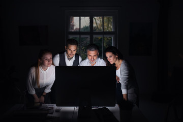 Group of businesspeople with computer indoors in office, working late.