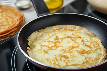 Delicious thin pancake in frying pan on induction stove, closeup