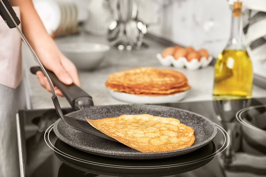 Woman cooking delicious thin pancakes on induction stove, closeup