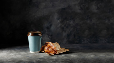 Fresh hot coffee in paper cup and sweet cake on dark mood background. 