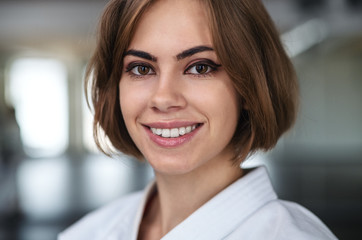 Young karate woman standing indoors in gym, looking at camera.