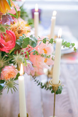 Festive table in boho chic style. Bouquet in a vase with fresh flowers of peonies, roses, eucalyptus. On a wooden table are burning candles in golden vintage candelabra.