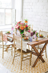 Festive table in boho chic style. Decorated with fresh flowers of peonies, lilies, succulents, eucalyptus. Cutlery and tableware on wooden table with candles in bronze candlesticks and Turkish sweets.