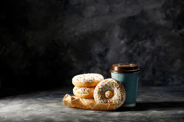 Fresh hot coffee in paper cup and sweet cake on dark mood background. 