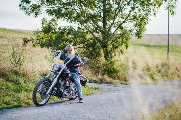 Obraz premium Starszy człowiek podróżujący z motocyklem na wsi. Skopiuj miejsce.