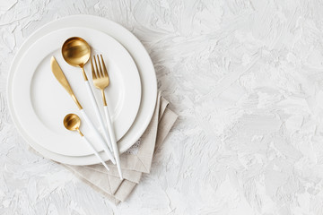 Beautiful gold and white cutlery on white plate on light white gray background - obrazy, fototapety, plakaty