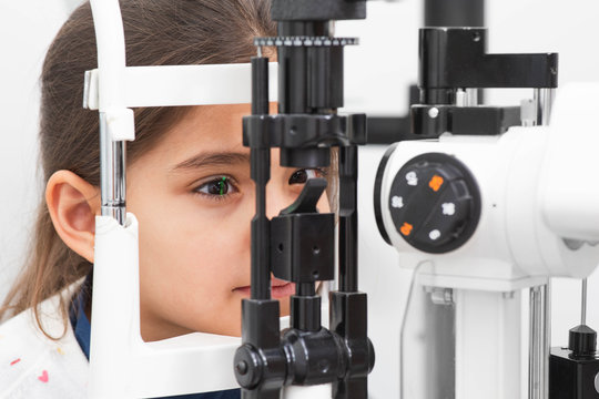 Little girl patient checking vision with special eye equipment. Girl getting eye exam at clinic, close-up