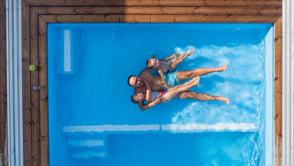 Top view of father with small children sitting in swimming pool outdoors.