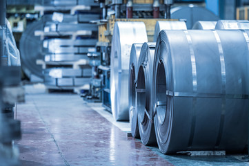 Industrial background. Big size steel coil stored inside industrial warehouse, blue toned image .