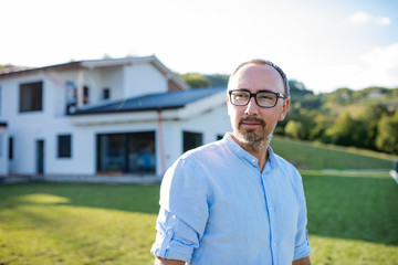 A portrait of man standing outdoors in garden by a house.
