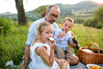 Father with two small children on meadow outdoors, having picnic.