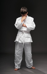 a sad teenager dressed in martial arts clothing having problem on a dark gray background, a sports concept