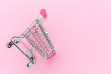 Small supermarket grocery push cart for shopping toy with wheels isolated on pink pastel colorful trendy background. Sale buy mall market shop consumer concept. Copy space.