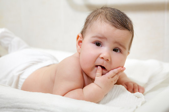 Warried Caucasian baby lying on his stomach with fingers in mouth, looking at camera