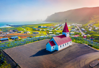 View from flying drone. Colorful evening scene of Vikurkirkja (Vik i Myrdal Church) with Reynisdrangar on background, Vik location. Wonderful summer view of Iceland.