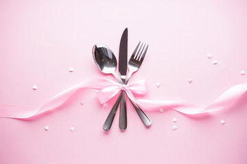 Sweet hearts and cutlery on a white plate with a pink ribbon on a pink background, flat lay. Valentine's Day. Mother's day background. Love concept.