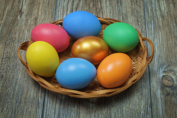 Obraz na płótnie Canvas Colorful Easter eggs in the basket on the brown wooden surface