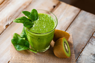 Healthy food, vegan diet concept - glass of fresh green juice or smoothie with kiwi, apple, spinach, banana. Antioxidant fresh detox beverage with raw ingredients.  Close up, wooden background
