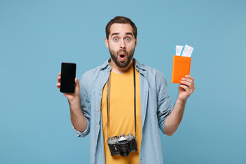 Shocked traveler tourist man in yellow clothes with photo camera isolated on blue background. Passenger traveling on weekends. Air flight journey. Hold passport tickets mobile phone with blank screen.