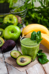 Healthy food and vegan diet concept - glass of fresh green juice or smoothie with kiwi, spinach, banana, avocado, apple. Antioxidant detox beverage with raw ingredients.  Copy space wooden background.