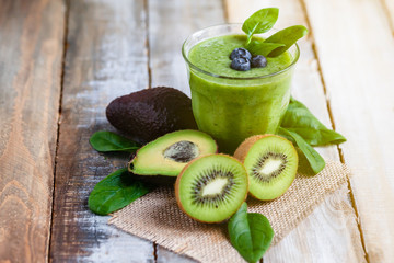 Healthy food and vegan diet concept - jar of fresh green juice or smoothie with kiwi, spinach, avocado, blueberry. Detox beverage with raw ingredients.  Close up, wooden background, copy space