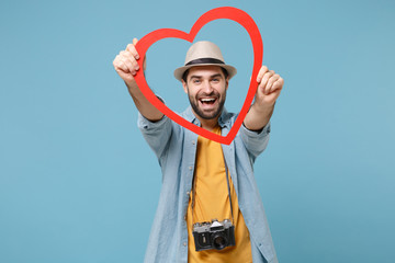 Laughing traveler tourist man in casual yellow clothes with photo camera isolated on blue background. Passenger traveling abroad on weekends. Air flight journey concept. Holding red big wooden heart.