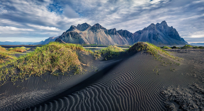 Awesome midnight sun view of Stokksnes cape with Vestrahorn (Batman Mountain) on background. Summer Icelandic landscape with black sand dunes with green grass. Travel to Iceland.