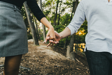 Close-up of the intertwined hands of a couple in love walking through a forest.
