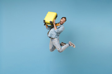 Fototapeta na wymiar Crazy traveler tourist man in yellow casual summer clothes isolated on blue background. Male passenger traveling abroad to travel on weekend. Air flight journey concept. Jump hold suitcase screaming.