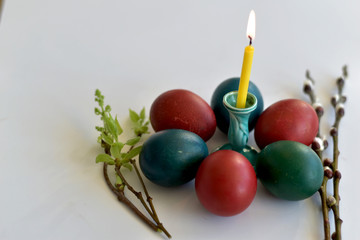 Easter eggs of different colors lie around a burning candle on the table.