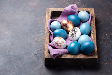 Festive blue Easter eggs in wooden box on dark background. Space for text.