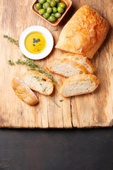 Ciabatta bread cutting, olive oil, thyme and green olives on a wooden board. Top view.