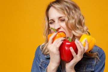 Fototapeta na wymiar Young girl in denim clothes isolated on yellow orange background in studio. Proper nutrition vegetarian food healthy lifestyle diet meal. Diabetes dieting concept. Eating biting colorful bell peppers.