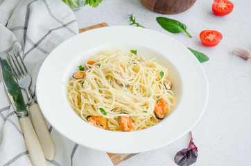 Pasta in a creamy sauce with mussels, cheese, garlic and parsley on a white plate on a light stone background. Rustic style. Horizontal orientation, top view