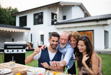 Portrait of people outdoors on family garden barbecue, taking selfie.