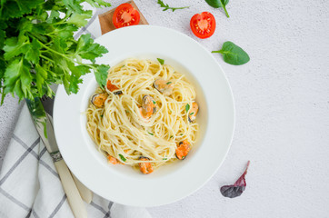 Pasta in a creamy sauce with mussels, cheese, garlic and parsley on a white plate on a light stone background. Rustic style. Horizontal orientation, top view, copy space