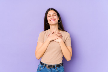 Young caucasian woman isolated on purple background laughing keeping hands on heart, concept of happiness.
