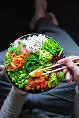 Vegan poke bowl with marinated watermelon, edamame, avocado, seaweed and carrot noodles. Man holding plate and chopstick
