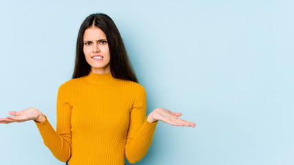 Young caucasian woman isolated on blue background confused and doubtful shrugging shoulders to hold a copy space.